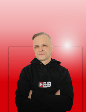 Mann mit kurzen Haaren und Hoodie steht mit verschränkten Armen vor einem roten Hintergrund.